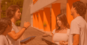Un grupo de cuatro jóvenes de la Universidad Anáhuac Veracruz se encuentra conversando animadamente en un entorno exterior, con un edificio de fondo que presenta colores naranjas