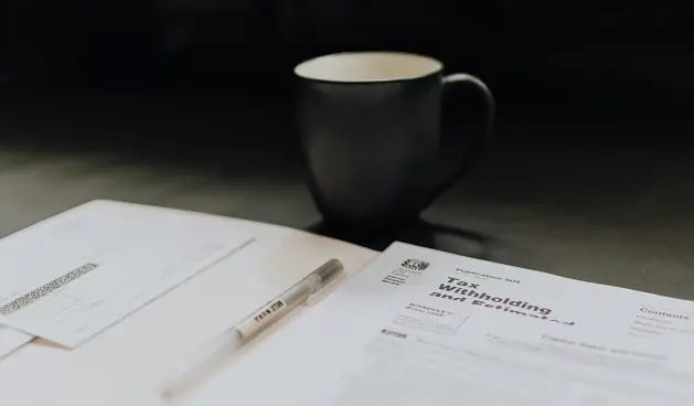 Papeles y pluma sobre una mesa con una taza.