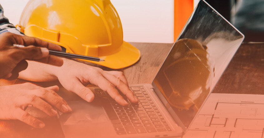 Profesionales de la construcción revisando planos en computadora portátil con casco de seguridad, ejemplo de oportunidades en sectores de empleo para ingeniería.