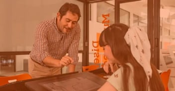 Profesor de diseño industrial asesorando a estudiante en proyecto digital con tableta gráfica, en aula creativa universitaria.