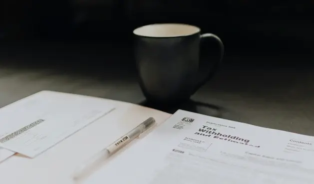 Papeles y pluma sobre una mesa con una taza.