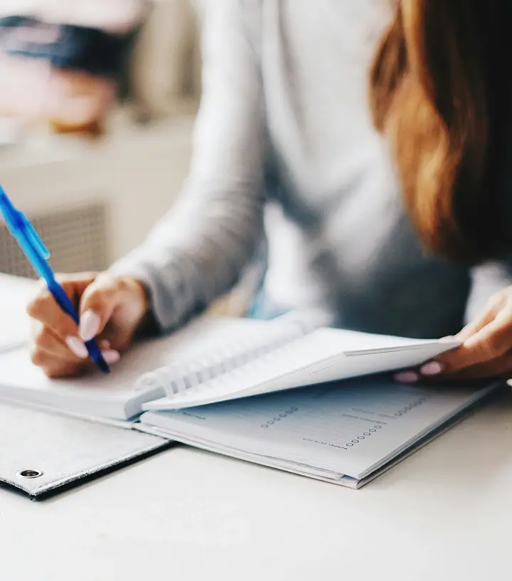 Mujer escribiendo con pluma en una libreta.