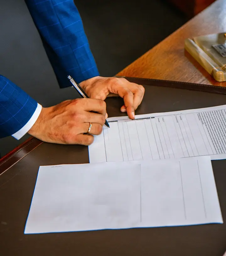 Persona firmando con pluma un papel.