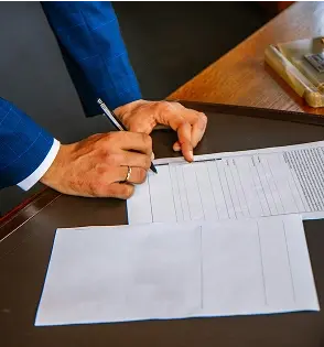 Persona firmando con pluma un papel.