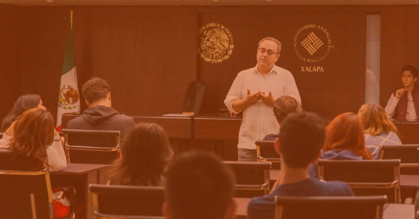 Clase magistral de Derecho en la Universidad Anáhuac Xalapa, con estudiantes atentos y profesor explicando en sala con emblemas oficiales de México.
