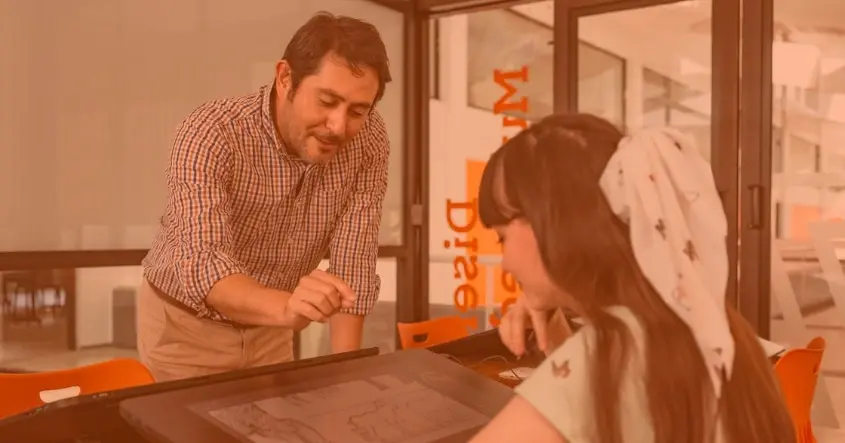 Profesor de diseño industrial asesorando a estudiante en proyecto digital con tableta gráfica, en aula creativa universitaria.
